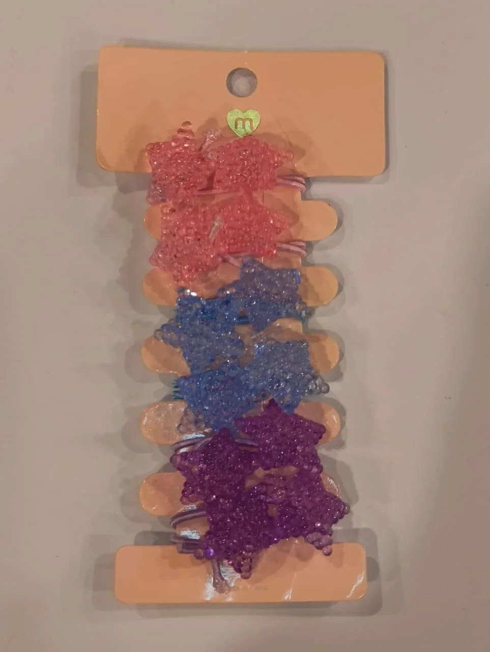 Set of colorful hair clips on a beige card with a visible brand logo.